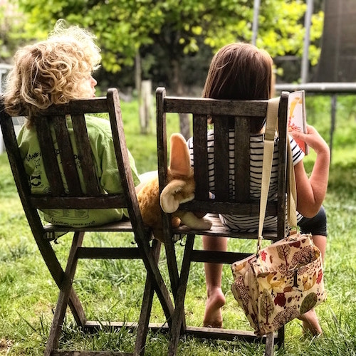 image from behind of two children outside in deckchairs reading a book